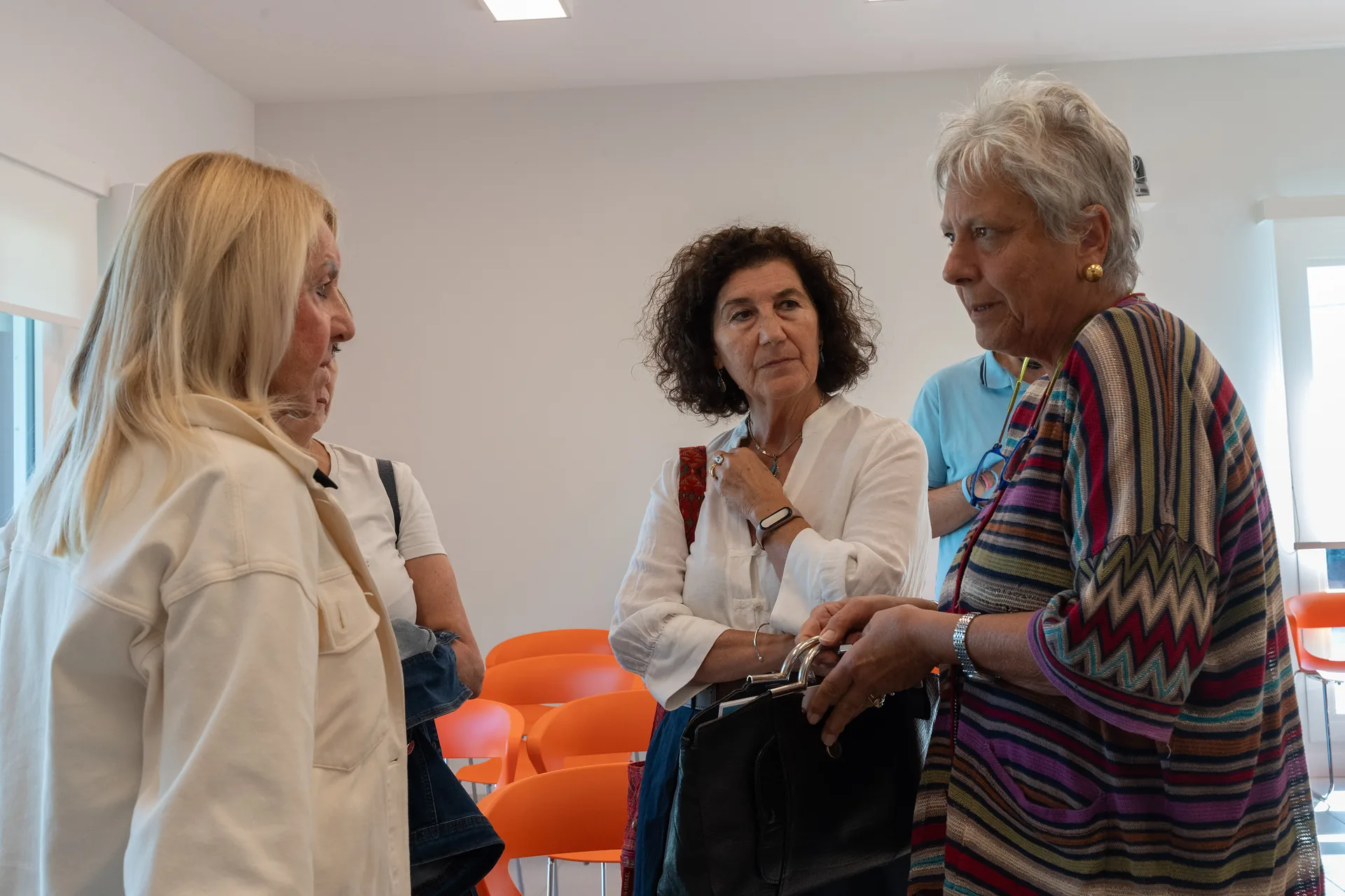 Tre partecipanti conversano in piedi tra le sedie della sala