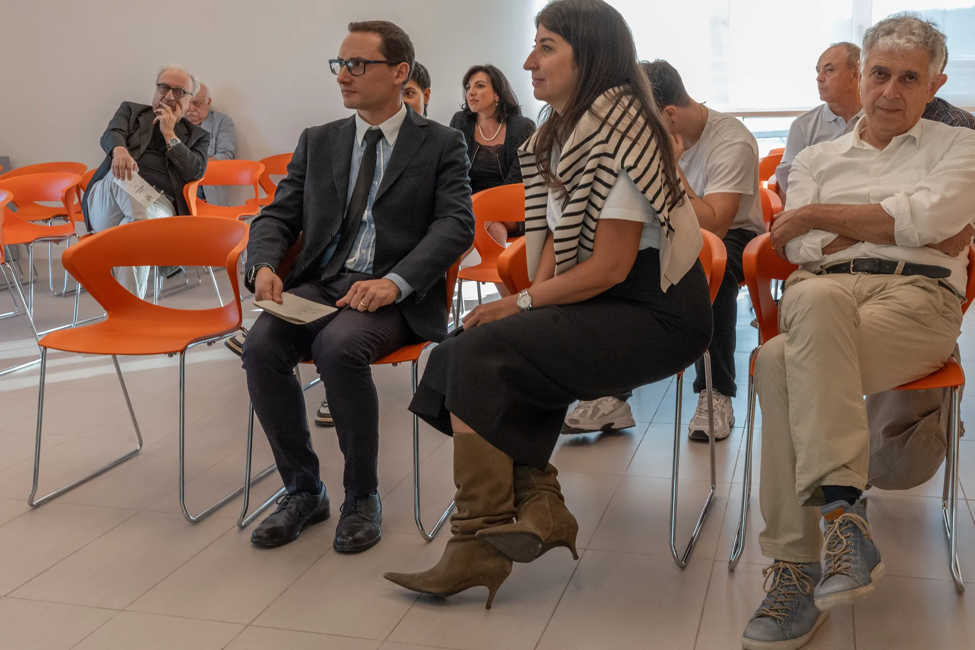 Partecipanti seduti sulle sedie arancioni ascoltano gli interventi