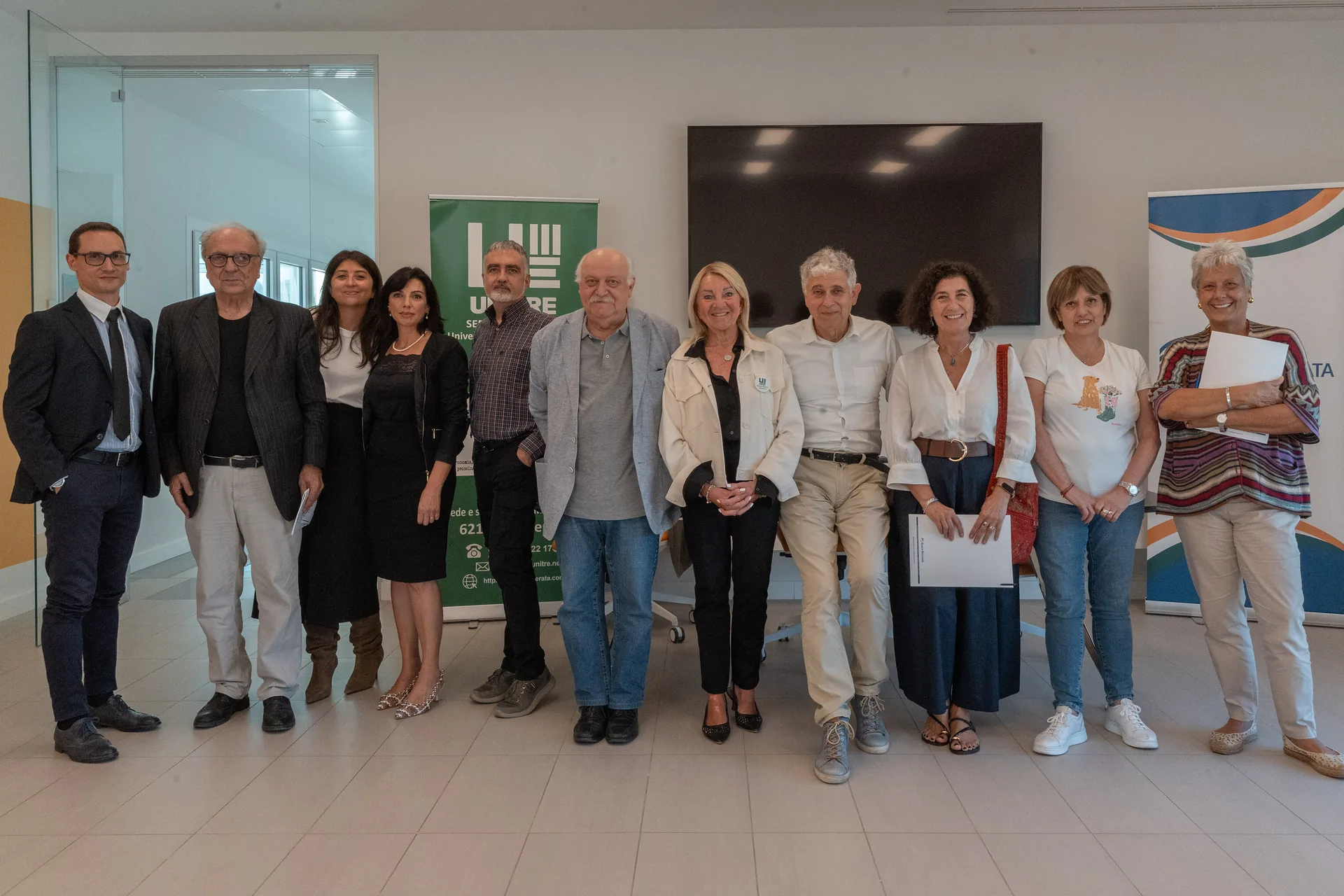 Foto di gruppo dell'Open Day di Unitre Macerata in Banca Macerata: persone in posa davanti al roll-up di Unitre